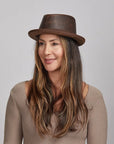 Woman with long brown hair wearing a brown leather hat and a beige top looking afar