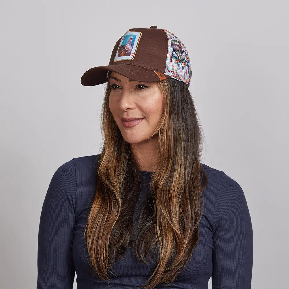 A woman with long brown hair,  wearing a brown Spirit cap and a navy blue top.