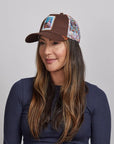 A woman with long brown hair,  wearing a brown Spirit cap and a navy blue top.