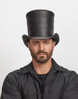 A man with stubble wearing a unique black stove piper hat and a black shirt.