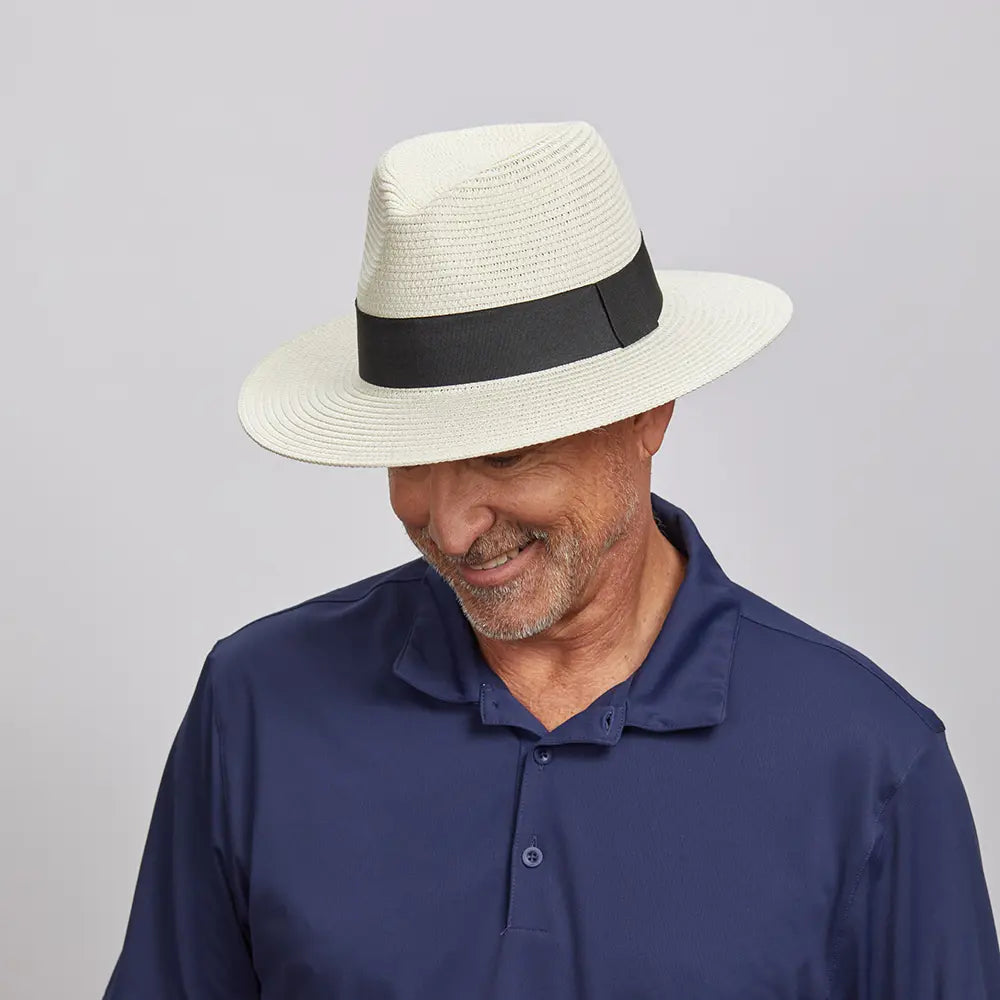 Middle-aged man smiling and looking down, wearing a Cream Afternoon Fedora Hat and a dark blue polo shirt.