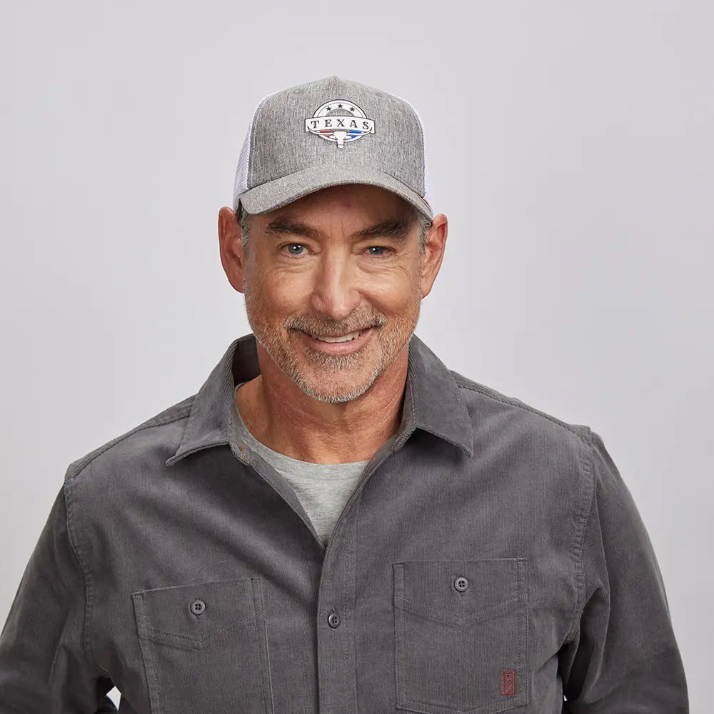 An older man wearing a gray Texas cap and a gray button-up shirt over a lighter gray t-shirt