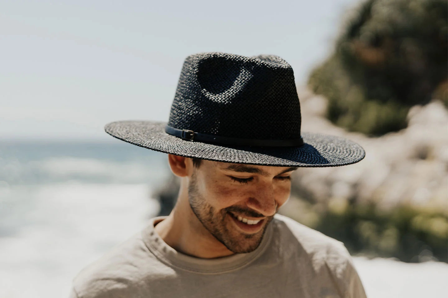 A man on the beach wearing a brown shirt and a black sun hat