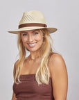 A smiling model wearing a brown sleeveless and a natural colored panama sun hat