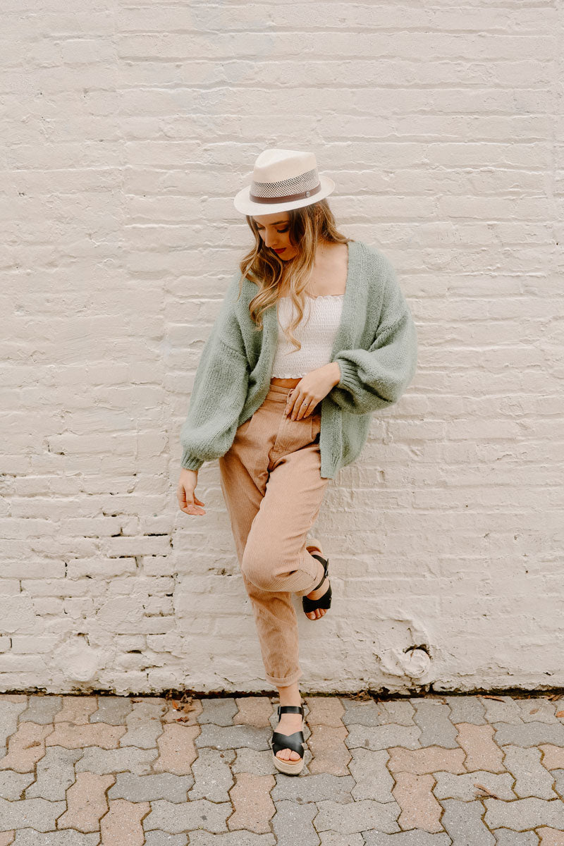 A woman leaning on a wall wearing tuscany cream sun hat