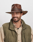 A smiling man looking to the side wearing a brown outback hat