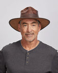 An old man wearing a grey top and a brown leather outback hat