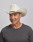 A man smiling and looking to the side wearing an ivory cowboy hat