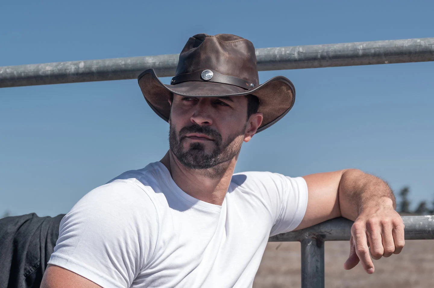 man in white leaning on a fence wearing a sun festival hat by american hat makers