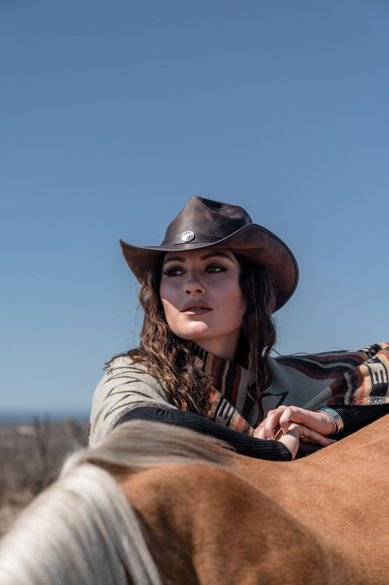 A woman leaning on a horse wearing a chocolate leather cowboy hat