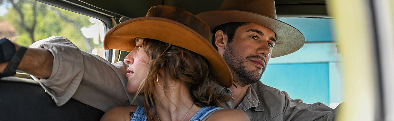 A man and a woman inside a car wearing brown felt hats