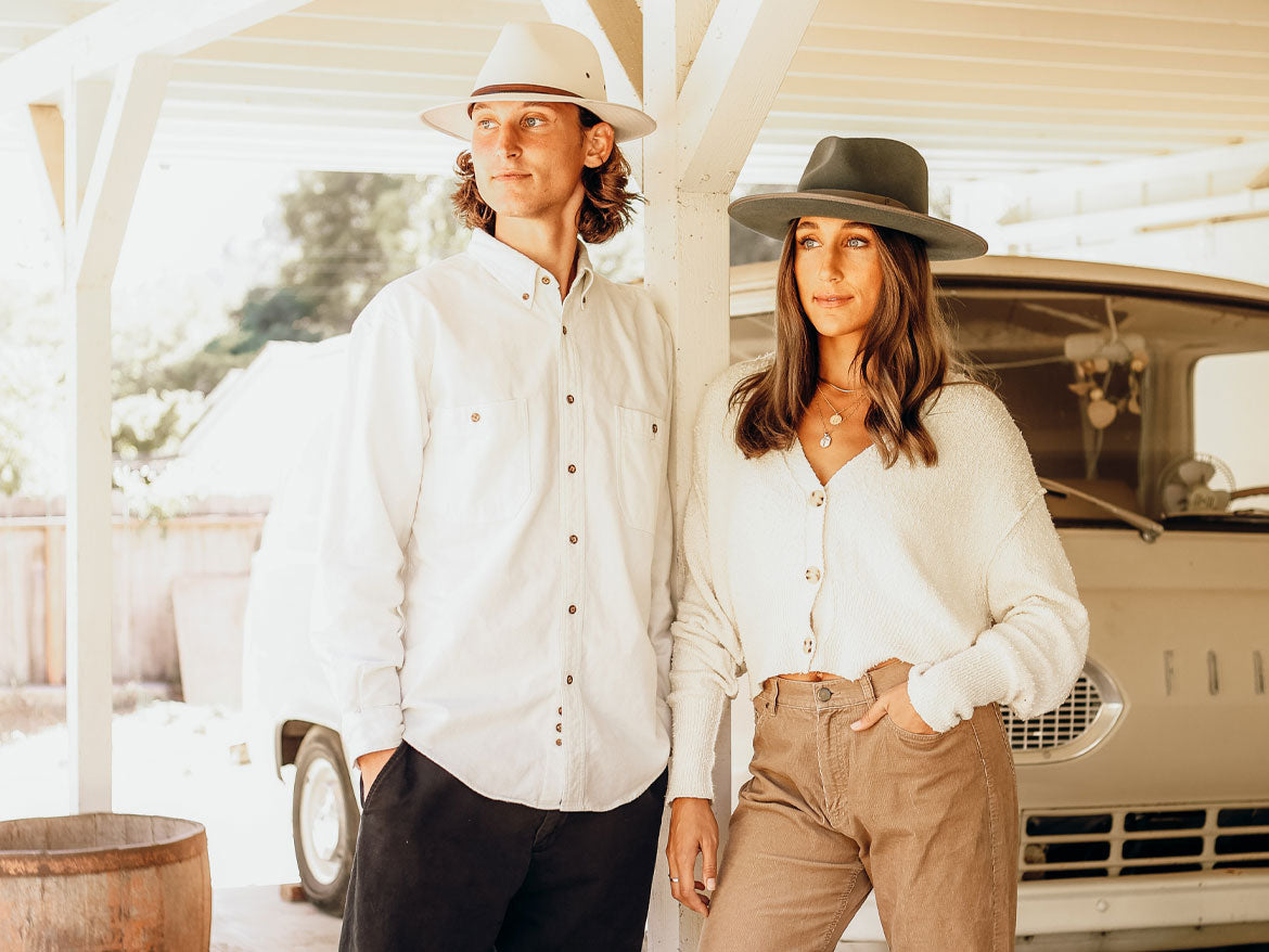 A man and a woman wearing a white top along with a felt hat and a white fedora