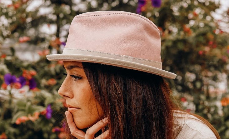 A woman sitting outdoors wearing a pink trilby hat