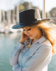 A woman on a boat facing side view wearing a black hat
