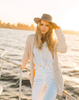 A woman on a boat lean on the metal steel and holding her hat
