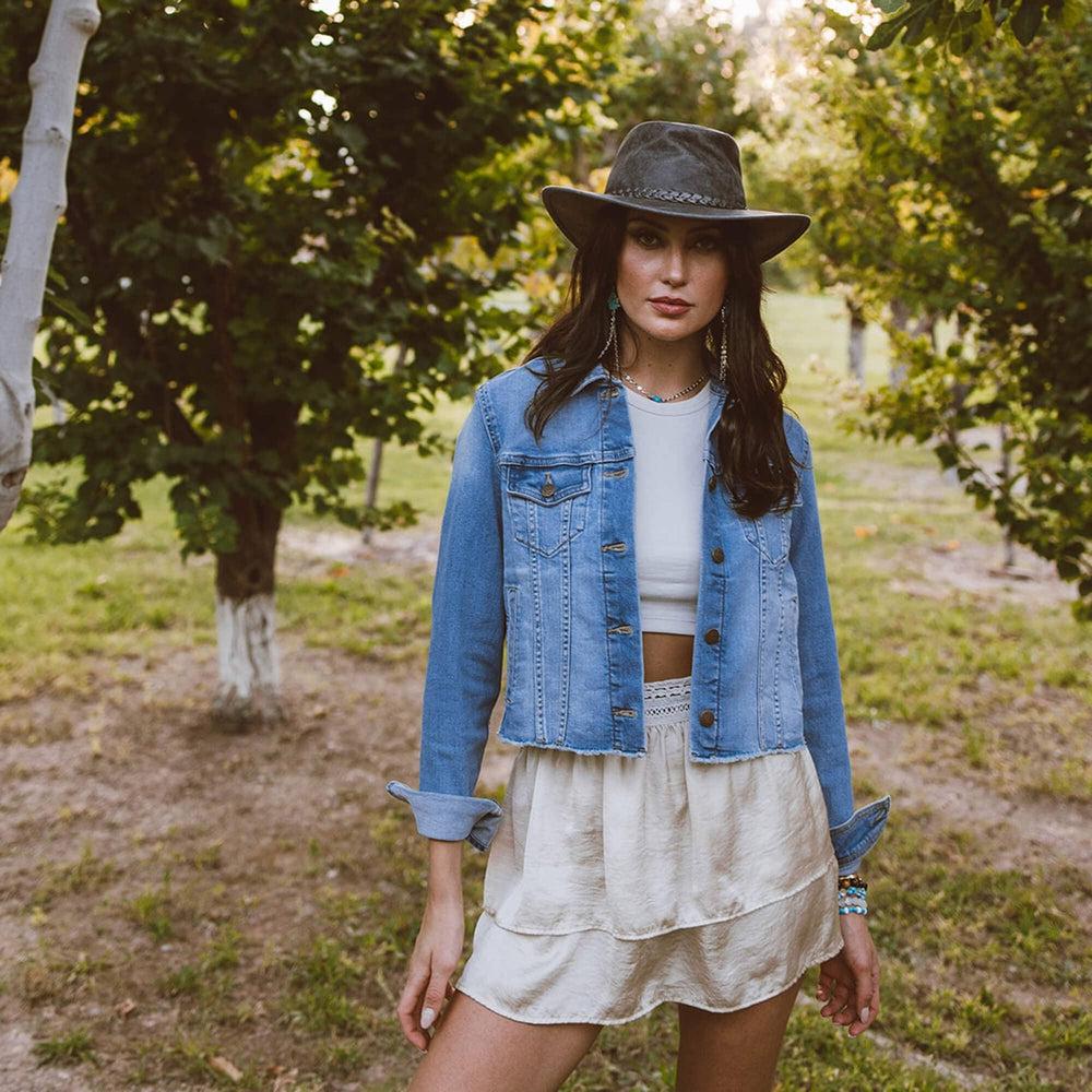 A woman standing outdoors wearing denim jacket and a Crusher Bomber Grey Outback Leather Hat 