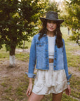 A woman standing outdoors wearing denim jacket and a Crusher Bomber Grey Outback Leather Hat