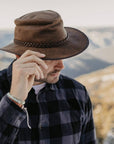 A man on a checkered polo wearing Crusher Bomber Brown Outback Leather Hat 