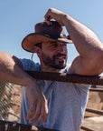 A man leaning on a steel fence wearing leader cowboy hat