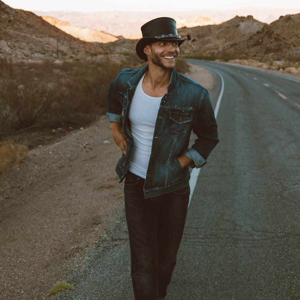 A man walking in the streets wearing El Dorado Black Leather Top Hat with a 5 Skull Band