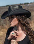 A woman standing outdoors wearing black leather cowboy hat