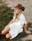 A man sitting on the grass wearing white dress and a Leather Cowboy Hat