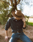 A man sitting on a tree wearing Hudson Bark Felt Fedora Hat