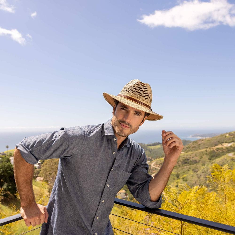 A man standing on a mountain view wearing Cubana Straw Sun Hat 