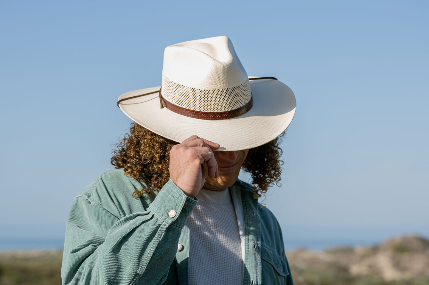 A curly haired man holding his cream Madrid sun hat