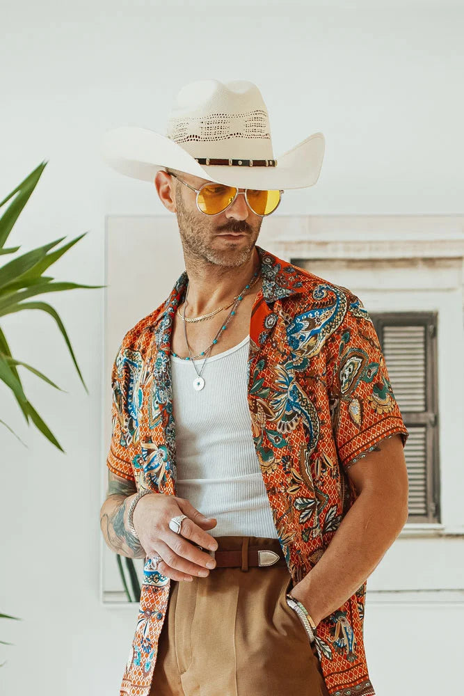 A man wearing a boho themed polo with sunglasses and a cream straw cowboy hat