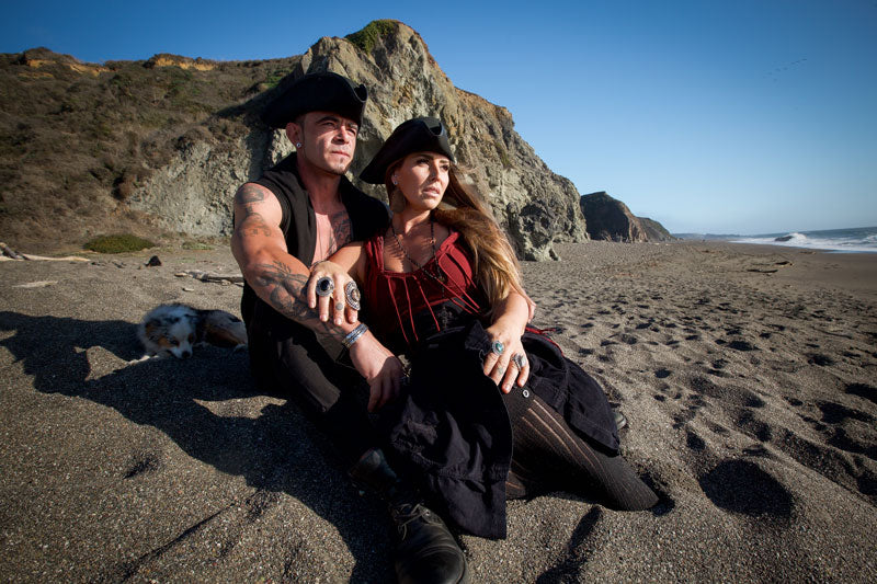 A man and woman with a dog on a seashore wearing top hats