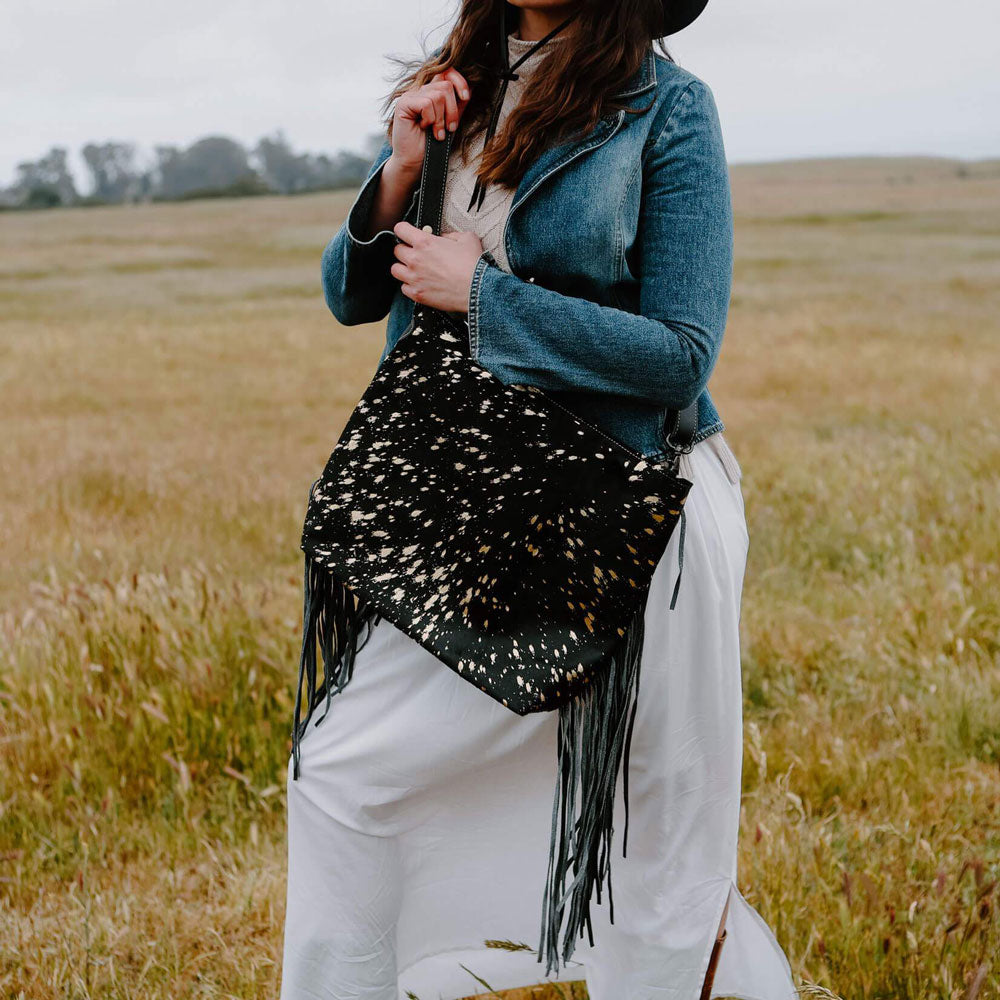 A woman walking in a field wearing a denim jacket and a black leather bag