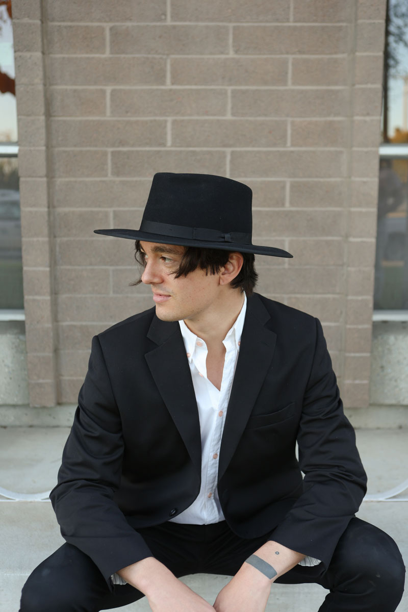 A man sitting outside a building wearing a suite and a black felt hat