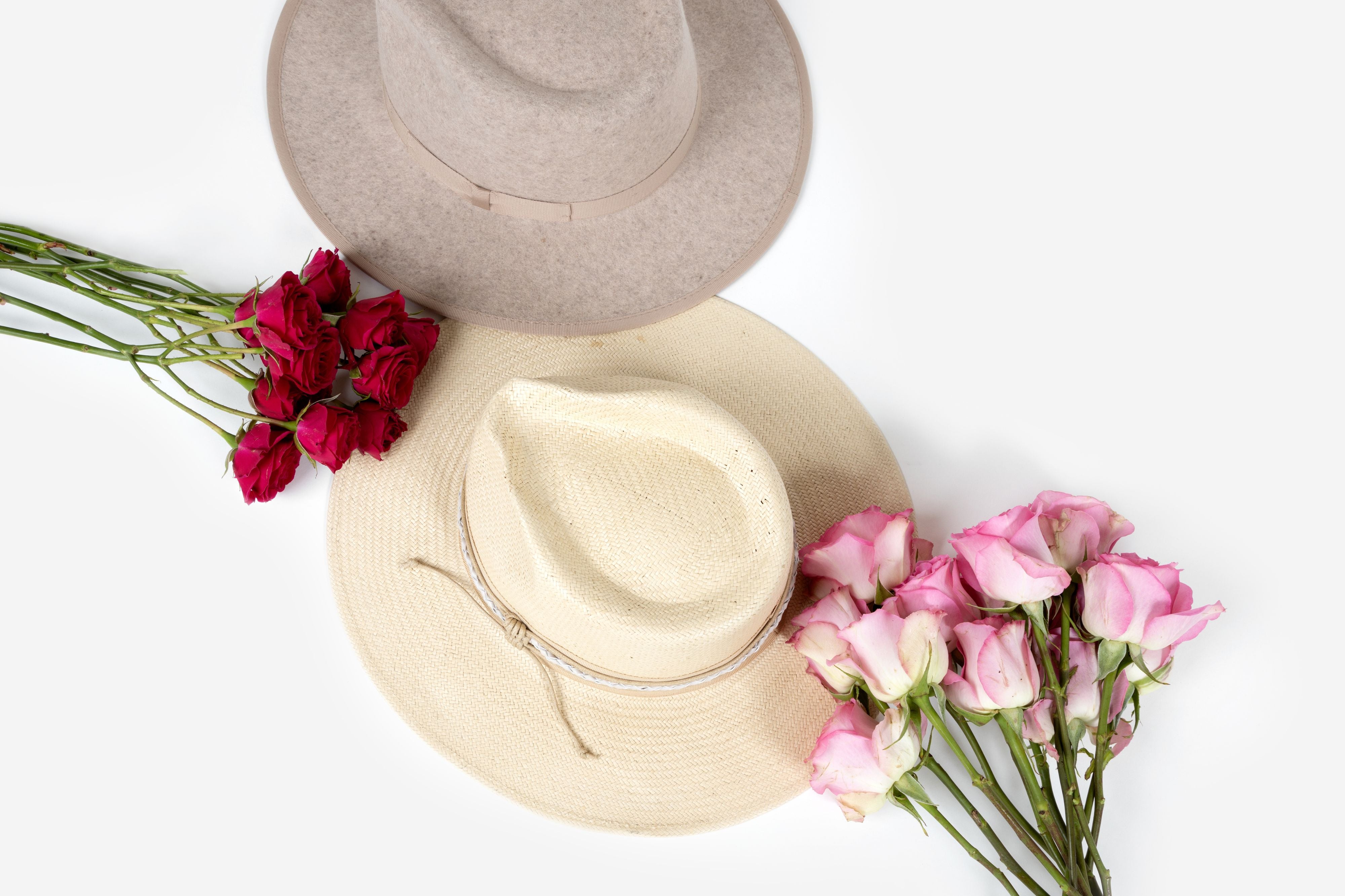 A top view of two felt hat beside red and pink flowers