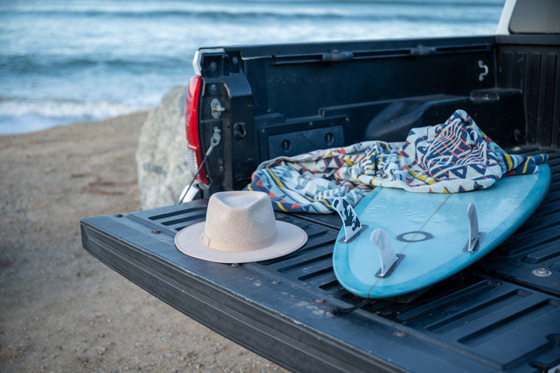 A felt fedora hat together with a surfing board placed on a truck in the beach
