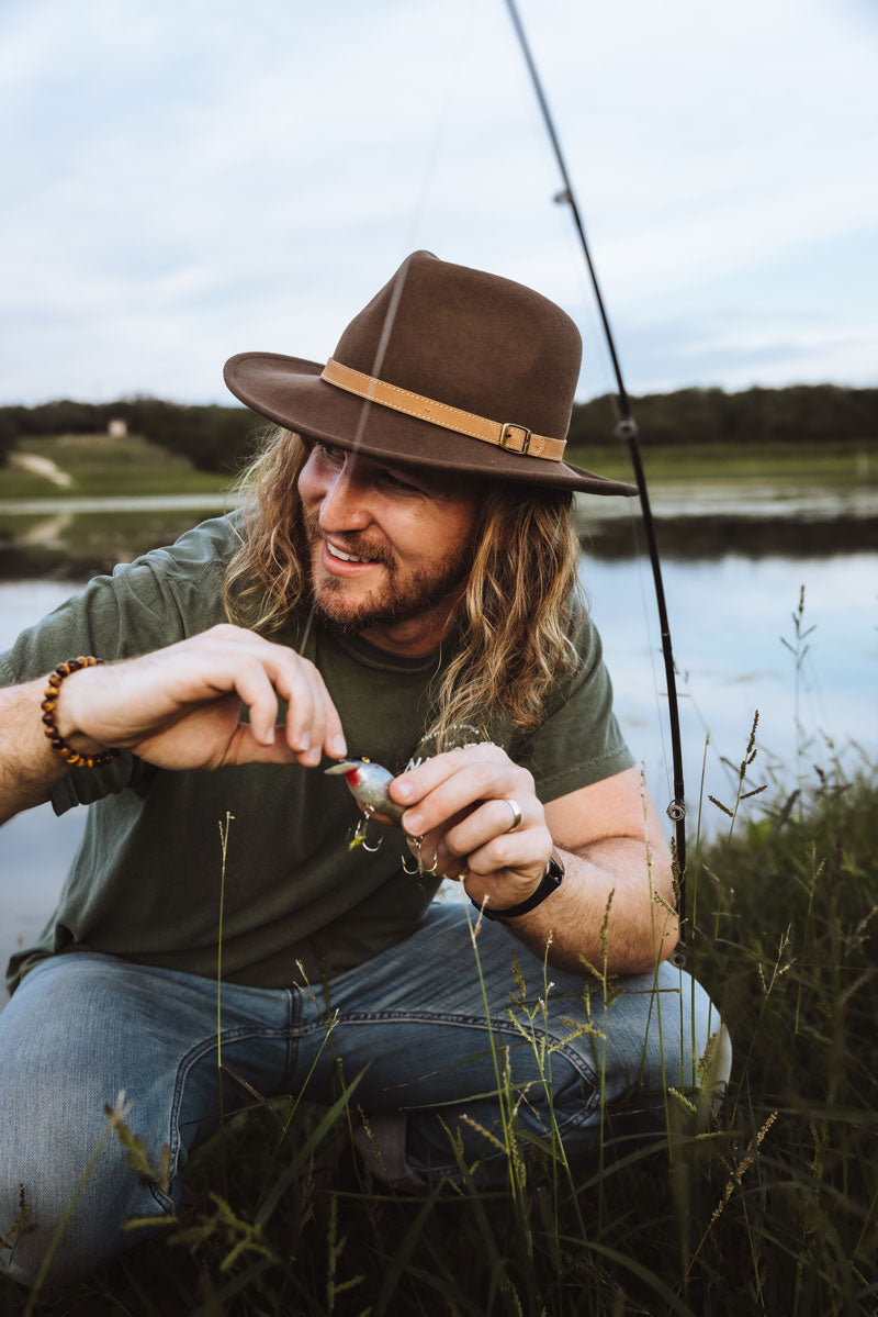 A man who goes fishing wearing a brown felt fedora hat