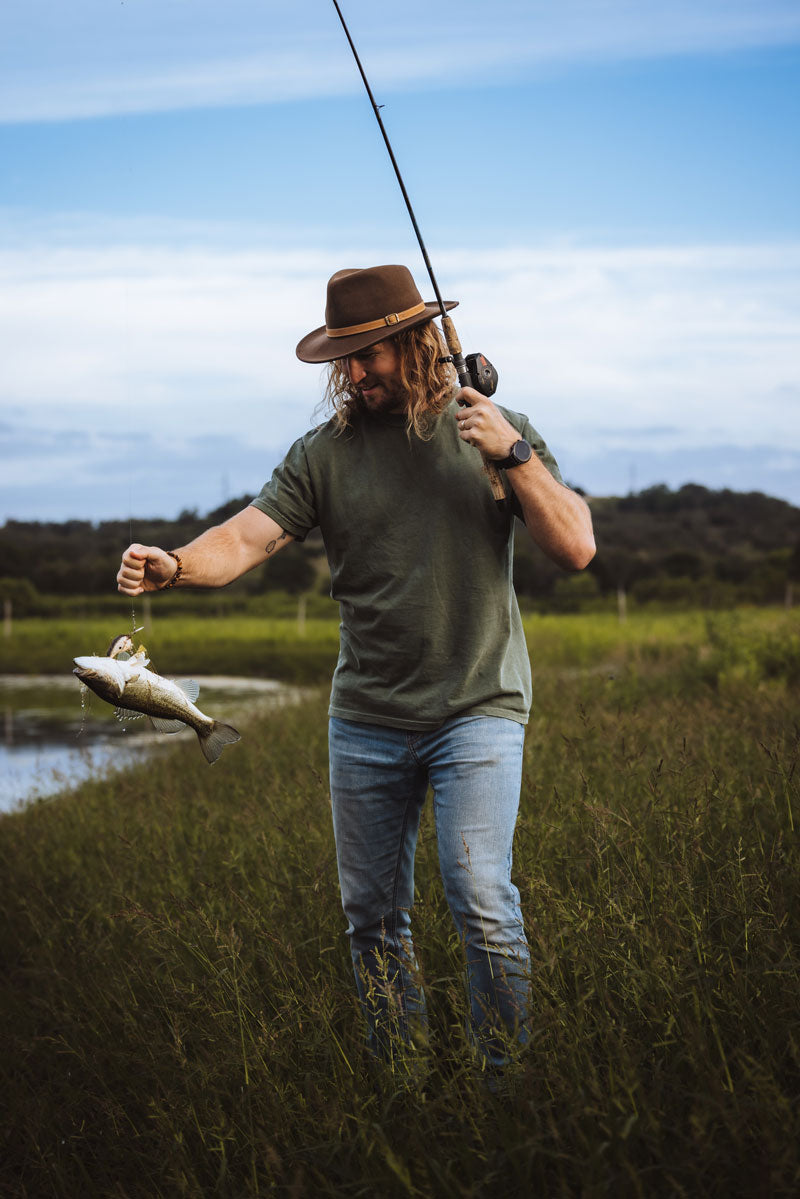 A man catching a fish wearing a brown felt fedora hat