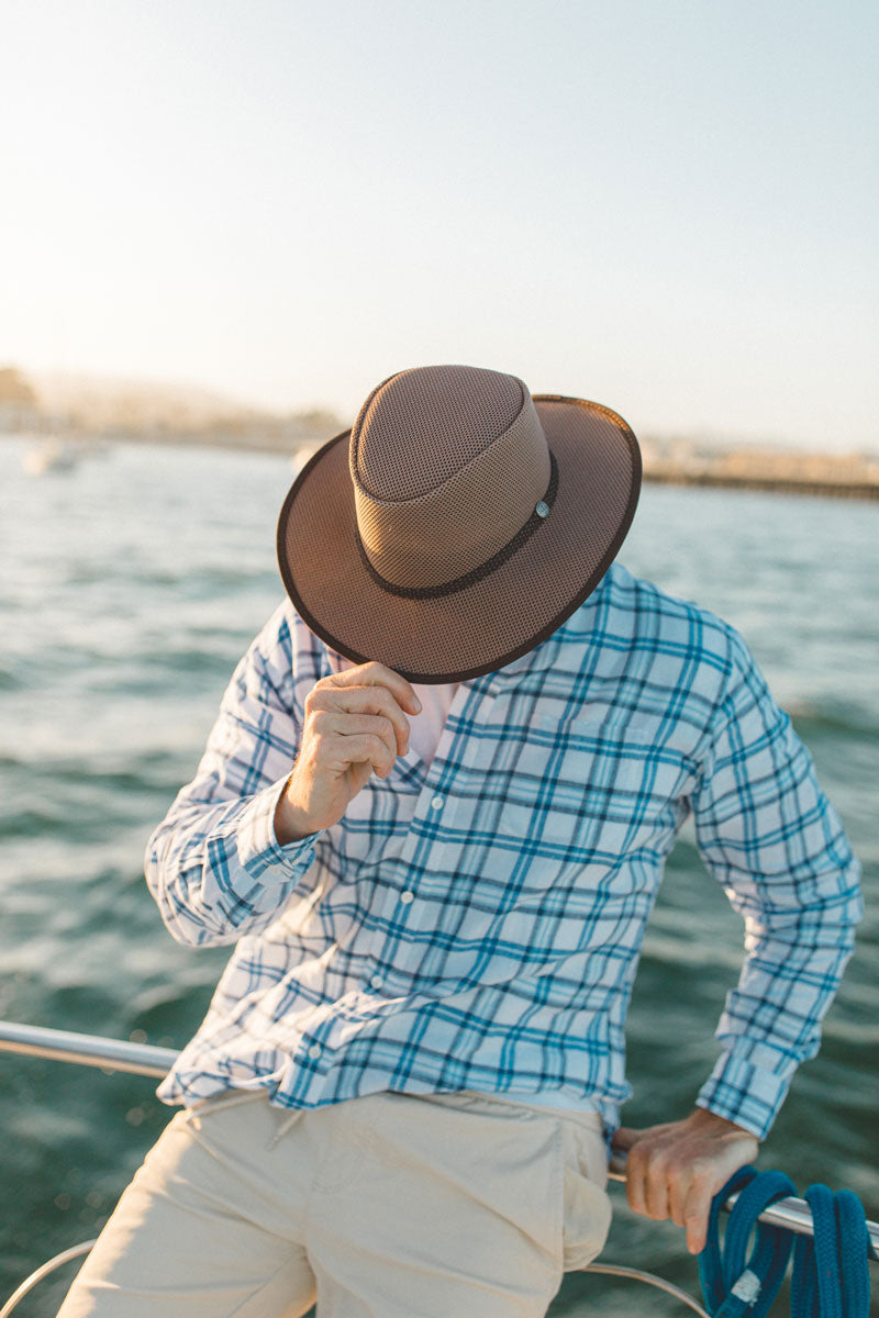 A man on a boat wearing a checkered blue polo and a cabana walnut sun  hat