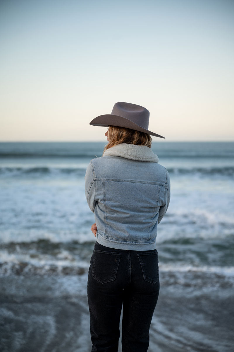 A woman on a shore wearing a felt cowboy hat