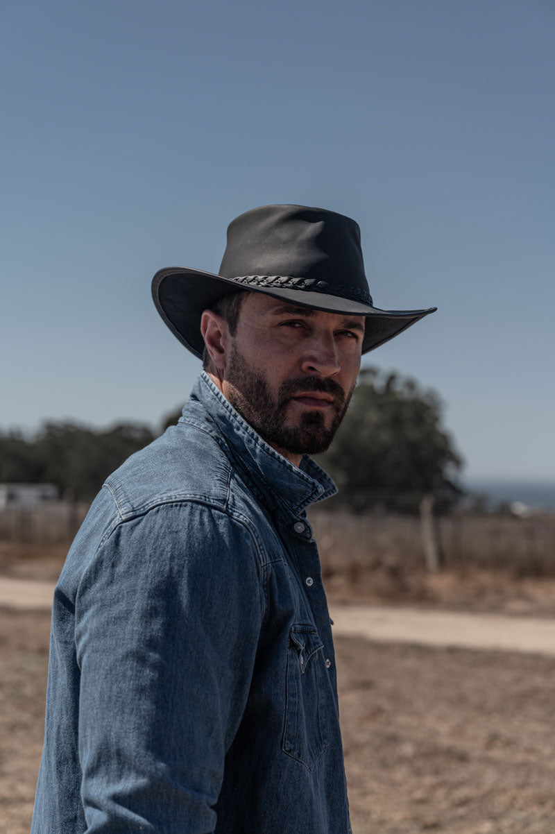 A man standing outdoor wearing a black leather hat