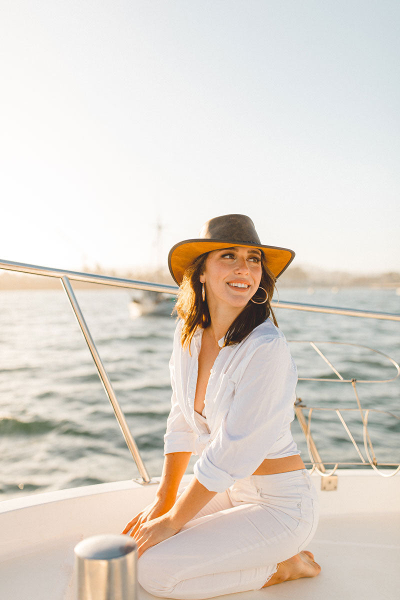 A woman squatting on a boat wearing a bomber brown leather hat