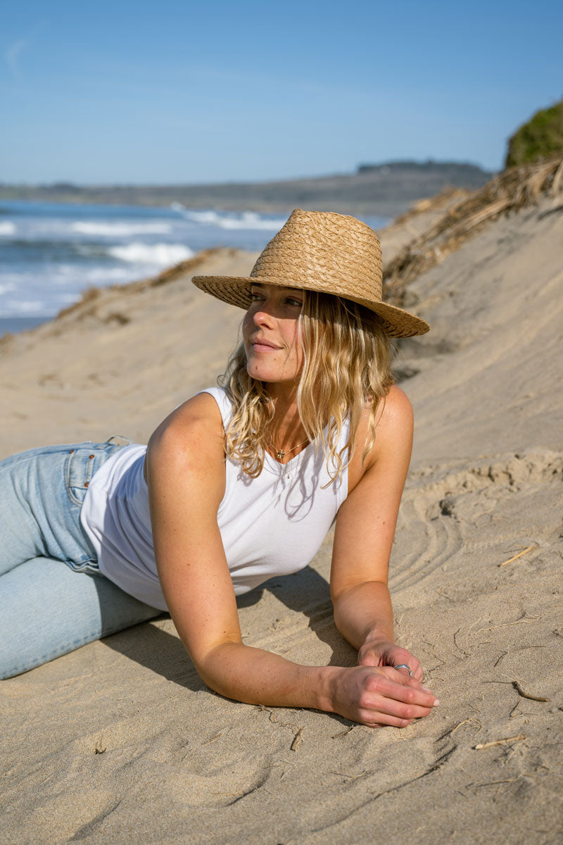 A woman on the beach lying on the sand wearing a straw sun hat