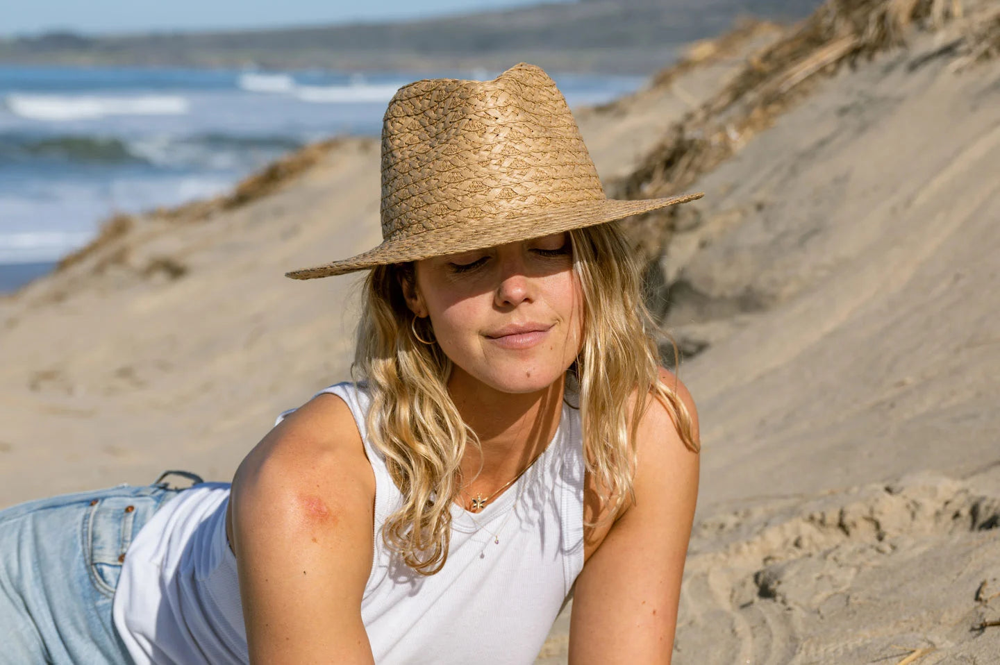 Woman laying at beach while wearing the Fabian straw sun hat by American Hat Makers