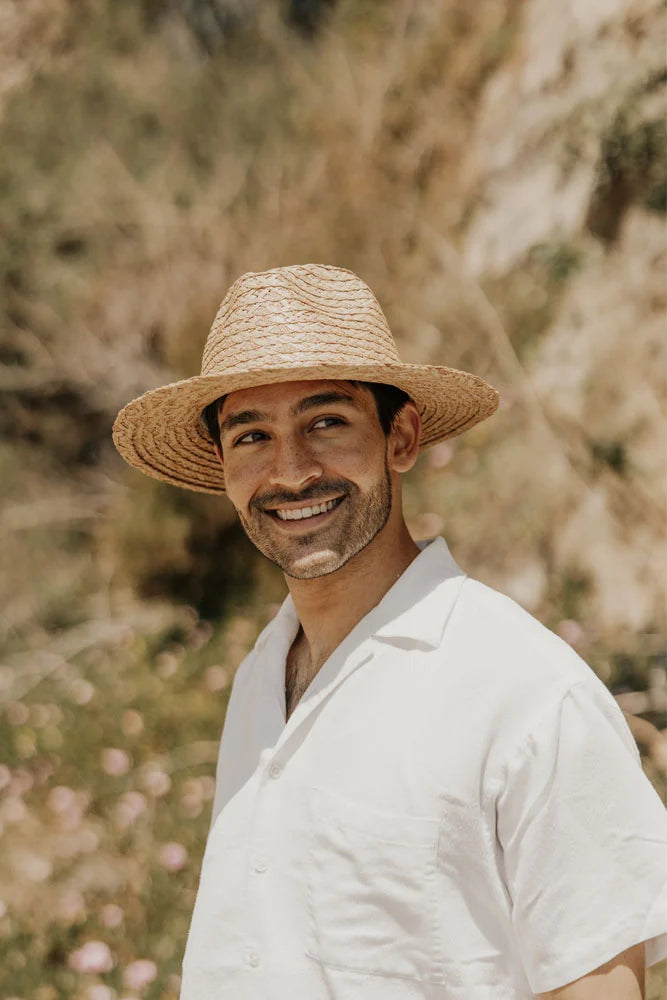 A man outdoors wearing a white polo and a straw sun hat