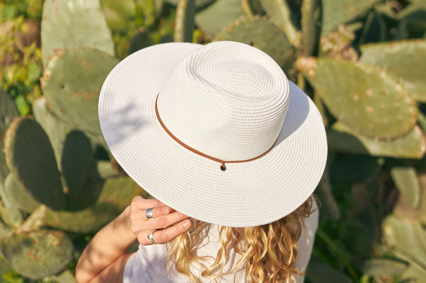 Woman sitting in cactus wearing the Felix white straw sun hat by American Hat Makers