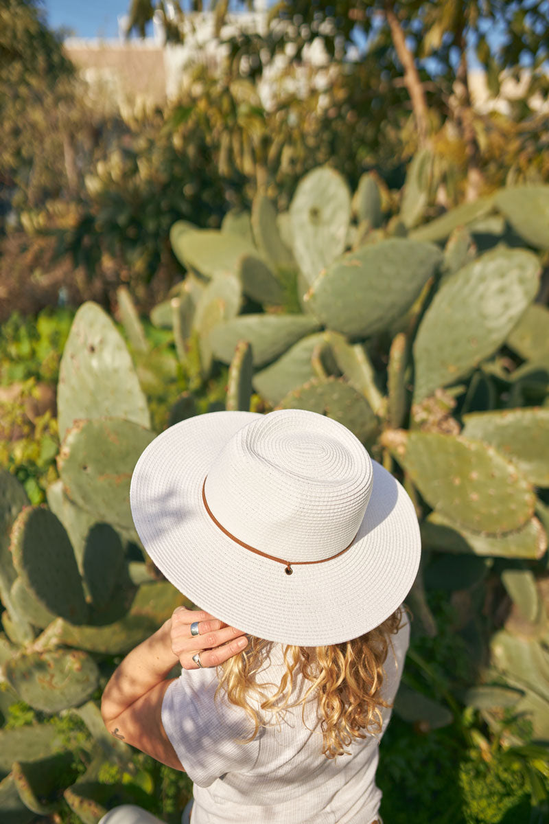 A woman in front of a cactus wearing a white straw sun hat