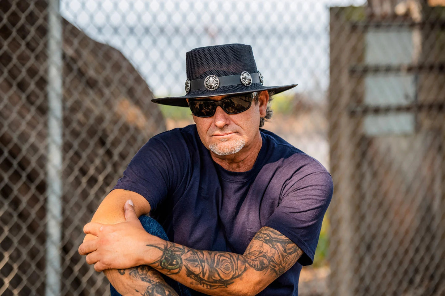 man with arm tattoos wearing a blue shirt and a black boater hat by american hat makers