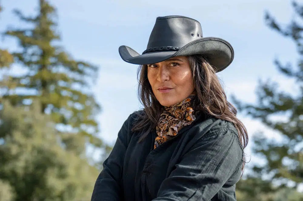 A woman wearing a black polo, scarf and a black leather cowboy hat