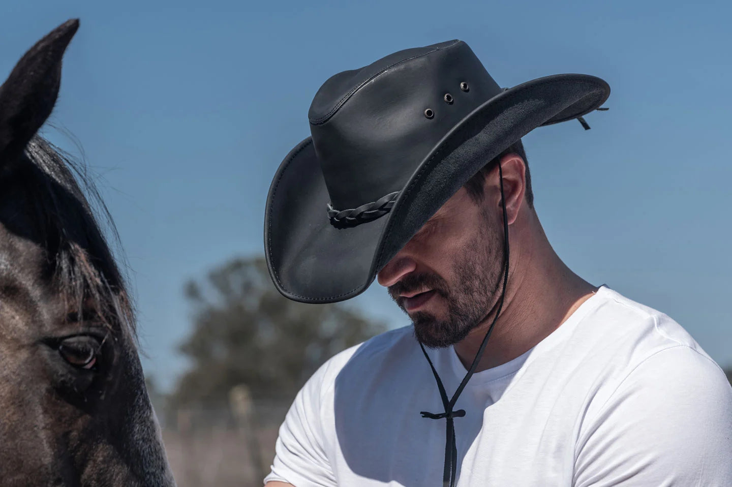 A man wearing a black leather cowboy hat with a chin strap