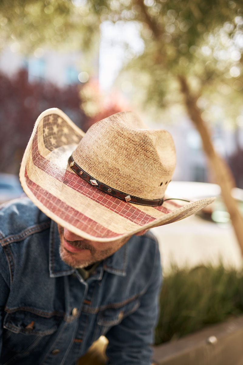 A man with a denim jacket wearing a straw cowboy hat